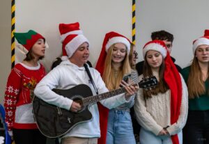 Grupa uczniów śpiewa przed innymi uczniami. Chłopak gra na gitarze.