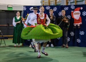 Dziewczyna w góralskim stroju tańczy. Za nią tańczy góral.