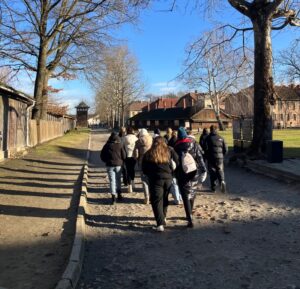 Uczniowie idą ścieżką wzdłuż budynków w obozie Auschwitz-Birkenau w Oświęcimiu