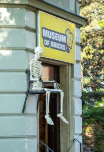 Wejście do muzeum klocków przy którym na zawieszonym na ścianie krześle siedzi wykonany z klocków szkielet człowieka.