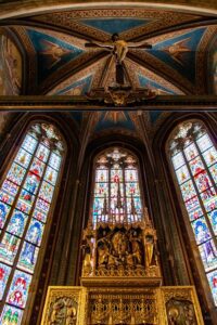 Widok na gotyckie witraże, sklepienie i krzyż prezbiterium praskiej katedry.