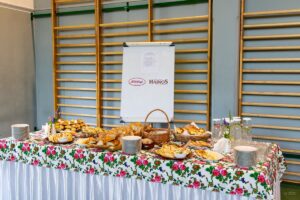 W rogu sali pięknie nakryty i zastawiony regionalnymi smakołykami stół, za którym umieszczony jest stojak z logo sponsorów.