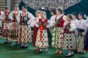 Muzyczny przerywnik występ zespołu regionalnego „ Mali Pyzowianie” na zdjęciu śpiewający uczniowie naj młodszych klas szkoły podstawowej.