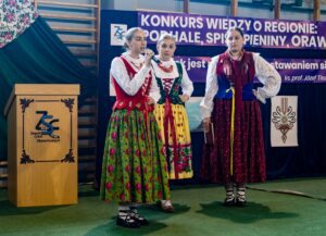 Zdjęcie trzech uczestniczek konkursu, z których jedna deklamuje wiersz twórcy ludowego.