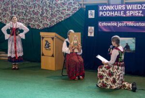 Scenka rodzajowa w wykonaniu trzech uczennic, z których jedna trzyma rekwizyt portret św. Kingi.