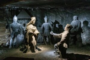 W podziemiach kopalni widok na solne rzeźby. Górnik klęczy i ofiaruje królowej Kindze grudkę soli.