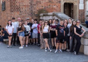 Cała grupa siedząc w rogu dziedzińca Collegium Maius słucha objaśnień Pani Przewodnik.