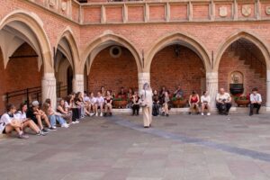 Cała grupa siedząc na schodach przy Collegium Novum słucha objaśnień Pani Przewodnik.