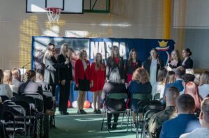 5. Przed zebranymi na scenie prezentuje się zespół wokalny złożony z dziewięciu uczennic w strojach galowych.