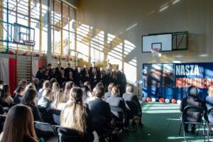 11. Zebrani zasłuchani oglądają występ chóru śpiewającego pieśni patriotyczne.