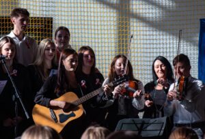 26. Drugie zbliżenie na śpiewających uczniów w chórze i grający na instrumentach.