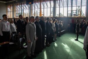 32. Zbliżenie na zaproszonych gości, którzy w postawie zasadniczej też śpiewają hymn narodowy.