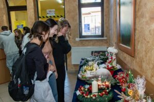 Trójka uśmiechniętych uczennic stojąc przed stołem ze stroikami zastanawia się nad wyborem.