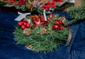 Zbliżenie na stroik w kształcie wianka z jedliny i czerwonych ozdób świątecznych.