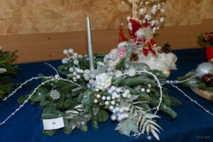 Zbliżenie na stroik wykonany na jedlinie i przyozdobiony białymi ozdobami i świecą.