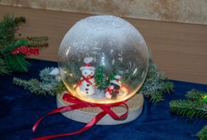 Zbliżenie na stroik w formie przeźroczystej bomki z bałwankiem w środku.
