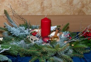 Zbliżenie na stroik z naturalnych gałązek jedliny z czerwoną świecą na środku.