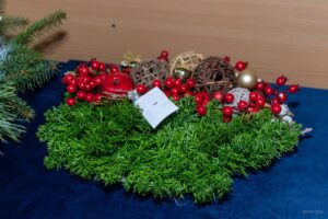 Zbliżenie na stroik w kształcie wianka wykonany z jedliny i przyozdobiony czerwonymi i złotymi ozdobami świątecznymi.