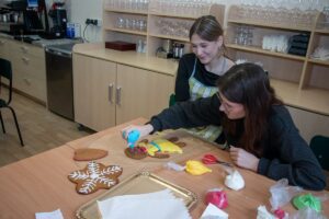 Dwie uczennicy zdobią piernikową dziewczynę.