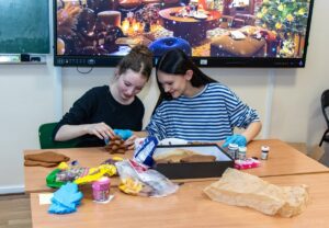 Dwie uczennice sklejają piernikową choinkę.