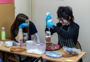 Uczennica wyciska biały lukier na piernikową pieramidkę.