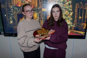 Na tle wyświetlonej prezentacji świątecznej dwie uczennice prezentują swoje dzieła.