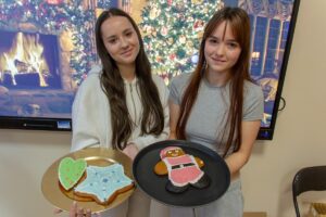 Na tle wyświetlonej prezentacji świątecznej dwie lekko usmiechające się uczennice prezentują swoje dzieła.