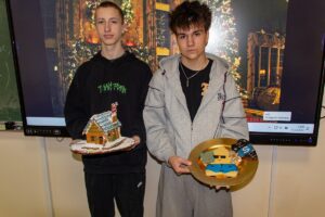 Na zdjęciu dwóch uczniów, którzy na tle wyświetlonej prezentacji świątecznej prezentują swoje dzieła.
