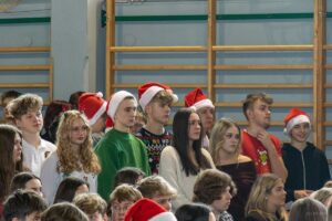 Grupa uczniów w czapeczkach mikołajowych z uwagą obserwująca występ starszej koleżanki.