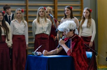 Zbliżenie na ucznia odgrywającego rolę króla, w tle część dziewcząt tworzących chór.