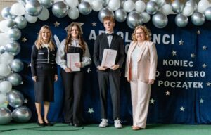 Na tle napisu dekoracyjnego uczniowie klasy 5 HOT wraz z wychowawczynią (stoi z lewej strony) i Pani Dyrektor ( stoi z prawej strony).
