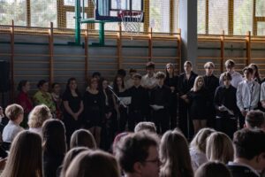Zbliżenie na stojących w głębi sali i śpiewających pożegnania uczniów klas IV.