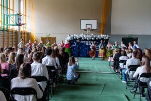 Część uczniów klas piątych stoi i radośnie macha ciesząc się ze świadectw ukończenia szkoły.