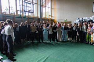 Uczniowie klas piątych w szeregu objęci rękami cieszą się z otrzymanych świadectw ukończenia szkoły.