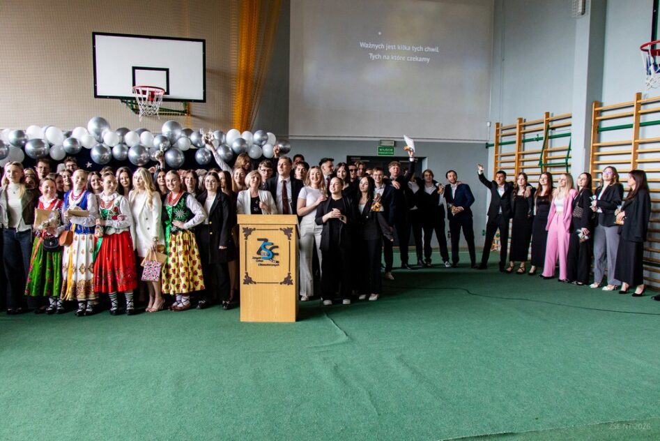 Część uczniów klas piątych stoi i radośnie macha ciesząc się ze świadectw ukończenia szkoły.