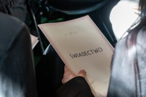 Ręka uczennicy trzyma w ręku ozdobną tekturowa teczkę z napisem świadectwo.