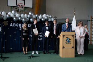 Przemawiający Pan Wicedyrektor wraz z dwoma absolwentami laureatami olimpiad przedmiotowych w asyście wychowawców i Pani Dyrektor.