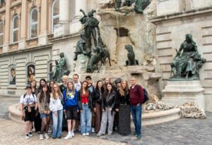 Zdjęcie grupy uczniów z nauczycielem przy fontannie.