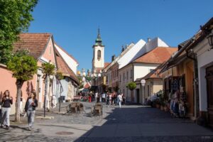 Widok na uliczkę małego miasteczka, po obu stronach parterowe budynki a w tle wieża kościoła.