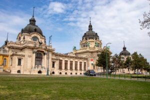 Na pierwszym planie piękny zielony duży trawnik a w tle ogromny. neobarokowy budynek budapesztańskich term.