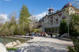 W tle ładny dziewiętnastowieczny budynek hotelu z ozdobną wieżyczką a przed hotelem na brzegu jeziora siedzi grupa uczniów.