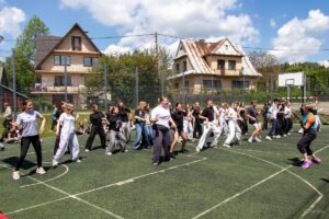 Taniec zumby - uczniowie w kilku szeregach naśladują ruchy prowadzącej pokaz nauczycielki.
