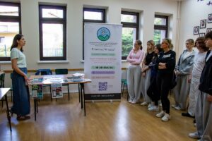 Grupa uczniów wraz z wychowawczynią stoją po prawej stronie słucha mowy pani z Ośrodka Interwencji Kryzysowej.